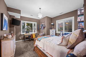 Carpeted bedroom featuring a chandelier and a desk
