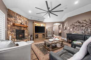 Living area with arched walkways, a fireplace, wood finished floors, vaulted ceiling, and a ceiling fan