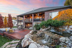 Back of property at dusk with brick siding, outdoor dining area, a shingled roof, a balcony, and a patio