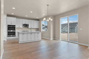Kitchen featuring white cabinetry, a kitchen island with sink, a chandelier, appliances with stainless steel finishes, and light wood finished floors