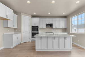Kitchen with recessed lighting, white cabinets, stainless steel appliances, light stone counters, and an island with sink