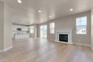 Unfurnished living room with recessed lighting, a textured ceiling, a glass covered fireplace, light wood-style flooring, and a chandelier