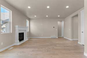 Unfurnished living room featuring recessed lighting, light wood-type flooring, and a glass covered fireplace