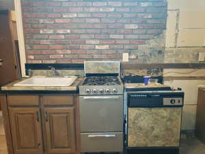 Kitchen with gas range oven, brick wall, and dark countertops