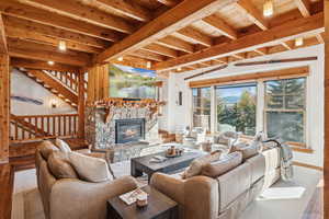 Living room featuring a stone fireplace, wood finished floors, a wood ceiling with exposed beams, and stairs
