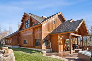 Rear view of house with roof with shingles, a yard, board and batten siding, and a wooden deck