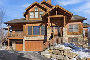 View of front facade with stone siding, roof with shingles, stairway, an attached garage, and covered porch