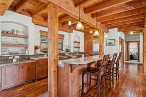 Kitchen with brown cabinetry, dark wood finished floors, a breakfast bar area, pendant lighting, and a wooden ceiling with exposed beams