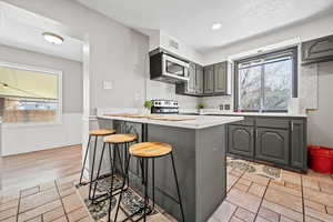 Kitchen with gray cabinets, a breakfast bar area, a peninsula, a textured ceiling, and appliances with stainless steel finishes
