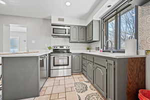 Kitchen with gray cabinetry, stainless steel appliances, a peninsula, light tile patterned floors, and backsplash