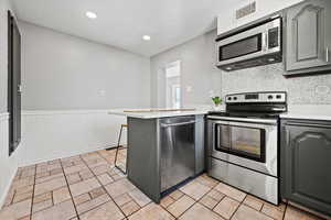 Kitchen featuring gray cabinets, a peninsula, stainless steel appliances, a wainscoted wall, and a breakfast bar area