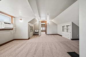 Additional living space with light colored carpet, a textured ceiling, vaulted ceiling, built in features, and cooling unit