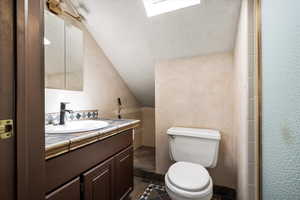 Full bathroom with a skylight, vaulted ceiling, vanity, and dark tile patterned flooring