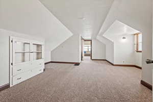 Additional living space with light carpet and vaulted ceiling