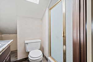 Bathroom featuring a stall shower, a skylight, vaulted ceiling, vanity, and stone tile floors