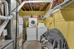 Laundry room with unfinished concrete flooring, heating unit, washer and dryer, and water heater