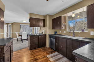 Kitchen with dark brown cabinetry, dark countertops, dark wood-style floors, and dishwasher