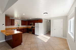 Kitchen featuring stainless steel appliances, light tile patterned floors, recessed lighting, a peninsula, and wooden counters