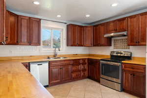 Kitchen with stainless steel appliances, backsplash, light tile patterned floors, under cabinet range hood, and recessed lighting