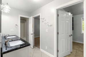 Bathroom featuring light tile patterned flooring, double vanity, light carpet, and a textured ceiling