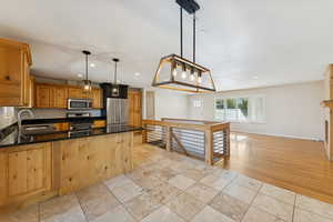 Kitchen featuring pendant lighting, stainless steel appliances, dark stone counters, recessed lighting, and brown cabinets