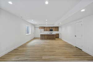 Kitchen with a kitchen island with sink, open floor plan, light wood finished floors, light countertops, and recessed lighting