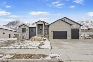 View of front of home featuring board and batten siding, a mountain view, stone siding, a garage, and driveway