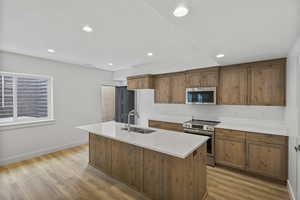 Kitchen with wood finish cabinetry, stainless steel appliances, a kitchen island with sink, light wood-style floors, and recessed lighting