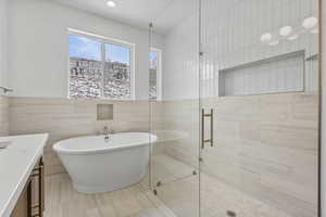 Bathroom with tile walls, vanity, a stall shower, and a freestanding bath