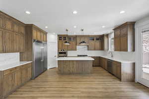 Kitchen featuring backsplash, a center island, stainless steel appliances, light wood-style flooring, and wood finish cabinets