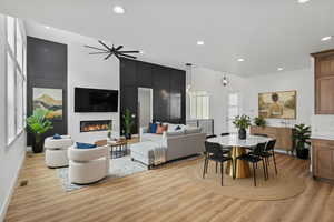 enhanced staging Living area with light wood-style flooring, a lit fireplace, a high ceiling, ceiling fan, and recessed lighting