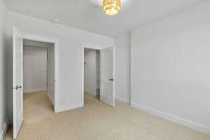 Unfurnished bedroom with a walk in closet and light colored carpet