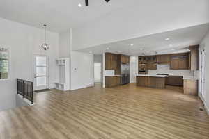 Unfurnished living room featuring light wood-style flooring, a high ceiling, and a chandelier