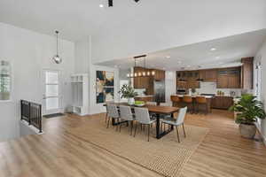 Enhanced staging Dining area with light wood-style flooring, suspended lighting, and a high ceiling