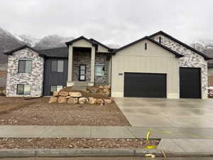View of front of property featuring stone siding, board and batten siding, concrete driveway, and a garage