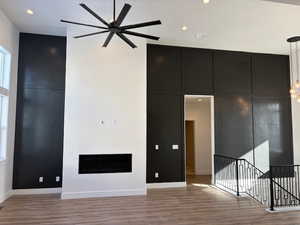 Unfurnished living room with a fireplace, recessed lighting, light wood-type flooring, a ceiling fan, and a high ceiling