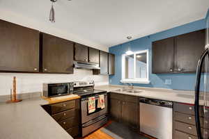Kitchen featuring black appliances, dark brown cabinets, pendant lighting, under cabinet range hood, and tasteful backsplash