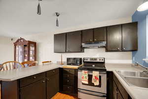Kitchen with a peninsula, electric stove, dark brown cabinetry, black microwave, and under cabinet range hood