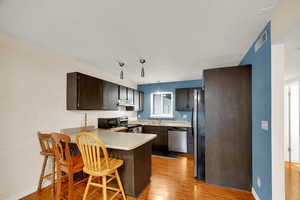 Kitchen featuring a peninsula, light wood-style flooring, a breakfast bar, appliances with stainless steel finishes, and light countertops
