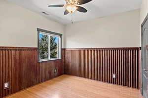 Unfurnished fourth bedroom with custom metal wainscoting, light wood-style floors, ceiling fan, and wood walls