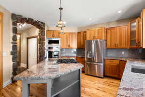 Kitchen featuring stainless steel appliances, a second island, wood flooring, hanging light fixtures, backsplash, and glass insert cabinets