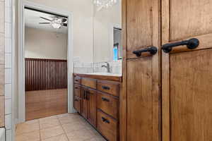 Shared bathroom featuring vanity, light tile patterned floors, wainscoting, tile walls, and ceiling fan