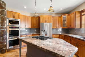 Kitchen featuring hanging light fixtures, a center island, stainless steel appliances, double ovens, stone countertops, and recessed lighting