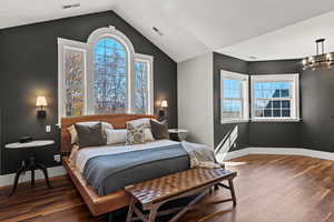 Primary bedroom with dark wood-type flooring, lofted ceiling, sitting area and a chandelier