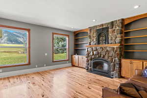 Family room featuring built-in shelves, light wood finished floors, a textured ceiling, a stone fireplace, recessed lighting and mountain views