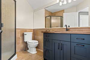Ensuite bathroom featuring a shower stall, tile walls, vanity, and wainscoting