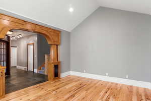 Front room featuring arched walkways with custom built-in shelves, wood finished floors, and high vaulted ceiling