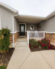 Doorway to property with stone siding, covered porch, and stucco siding