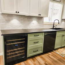 Kitchen with green cabinets, beverage cooler, dishwasher, decorative backsplash, and white cabinets