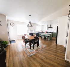 Dining area with dark wood-type flooring, lofted ceiling, a chandelier, and a textured ceiling
